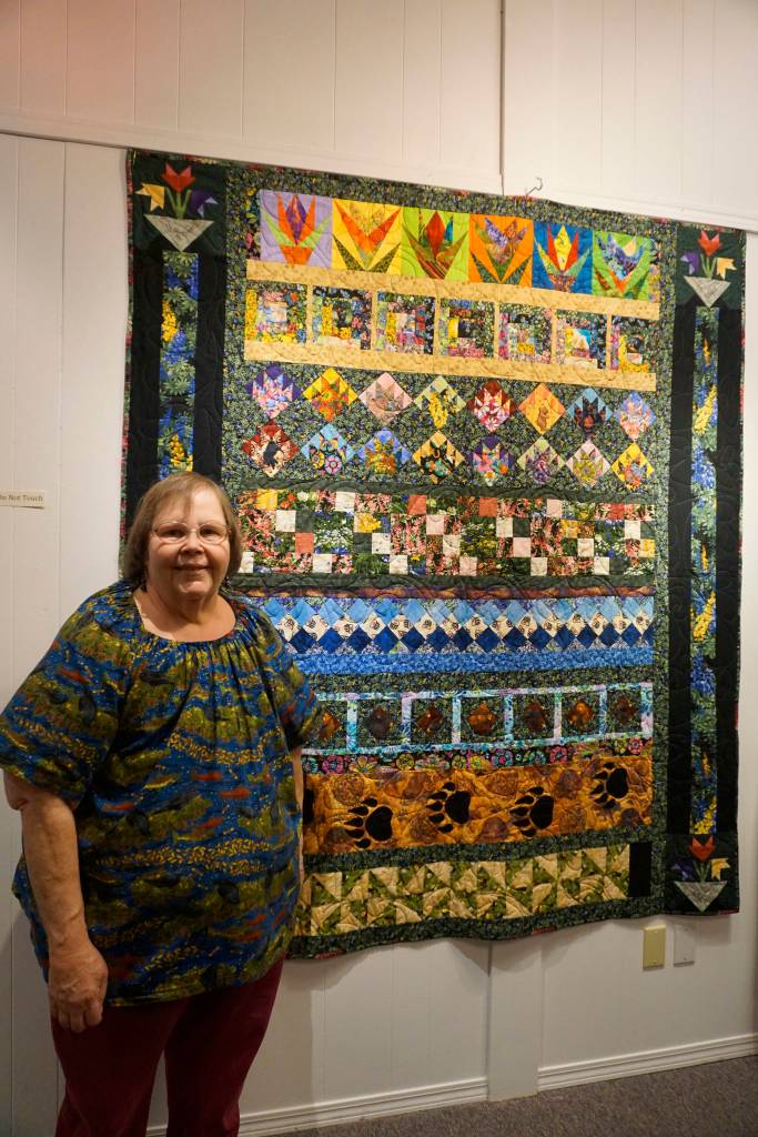 Linda Wagner stands by her Bears and Flowers quilt, quilt, one of the works in the 9 Women / 9 Quilts show that opened last Friday, Feb. 1, 2019, at the Homer Council on the Arts, in Homer, Alaska. (Photo by Michael Armstrong/Homer News)