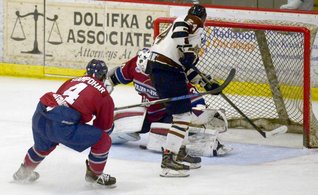 Kenai River Brown Bears forward Zach Krajnik slips the puck through the legs of Fairbanks Ice Dogs goalie Nate Reid in front of Ice Dogs defenseman John Stampohar on Friday, March 22, 2019, at the Soldotna Regional Sports Complex. The short-handed goal was the game-winner. (Photo by Jeff Helminiak/Peninsula Clarion)