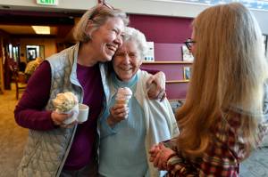 In this March 8, 2019 photo, Margie Beedle, left, hugs her mother, Sally Thibodeau, as they chat with Alaska Pioneer Home employee Laura Minne during the homes weekly ice cream social. (Michael Penn | Juneau Empire File)