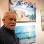 Bill Smith stands by a John Fenske painting, top, that his children bought for him. Fenskes retrospective show opened on First Friday, April 5, 2019, at Kachemak Bay Campus in Homer, Alaska. (Photo by Michael Armstrong/Homer News)
