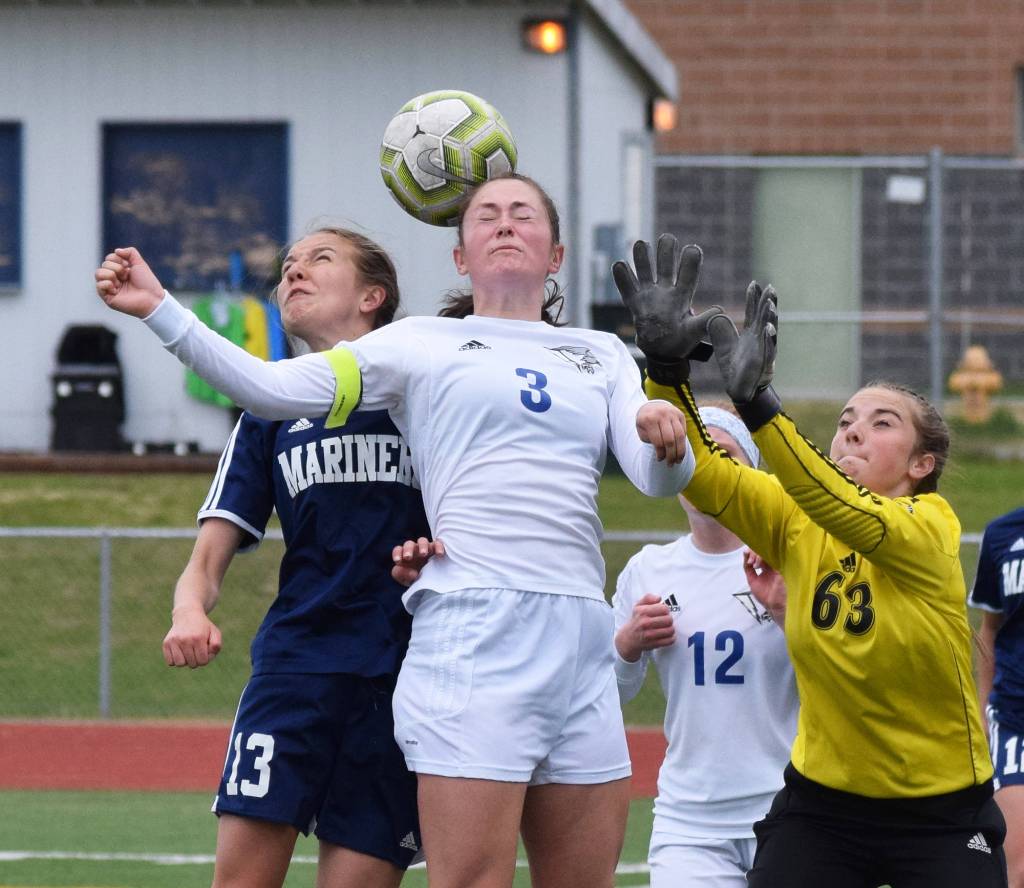 Homers Kappa Reutov (left) jumps for a header against Thunder Mountains Macey Fuette and Thunder Mountain goalkeeper Sam Dilley, Thursday, May 23, 2019, at the Div. II state soccer championships in Eagle River. (Photo by Joey Klecka/Peninsula Clarion)