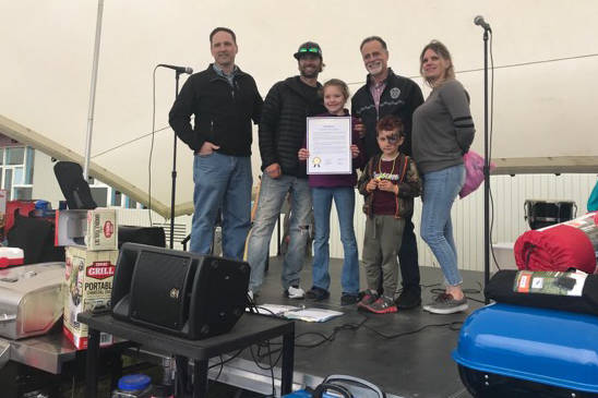 Rep. Ben Carpenter, R-Nikiski, left and Sen. Peter Micciche, R-Soldotna, center right, pose for a photo with Kaydence Jeffereys, center, and her family after honoring her victory at a recent wrestling championship during the Family Fun in the Midnight Sun festival at the North Peninsula Recreation Center in Nikiski, Alaska on June 15, 2019. (Photo courtesy Richard Best)