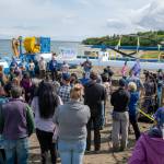 In this Tuesday, July 16, 2019, photo released by the Alaska Governors office, Gov. Mike Dunleavy, center rear, speaks in front of a Riv-Gen Power System turbine on the bank of the Kvichak River in Igiugig, Alaska. A tiny Alaska Native village is adopting an emerging technology to transform the power of a local river into a renewable energy source. (Austin McDaniel/Alaska Governors Office via AP)