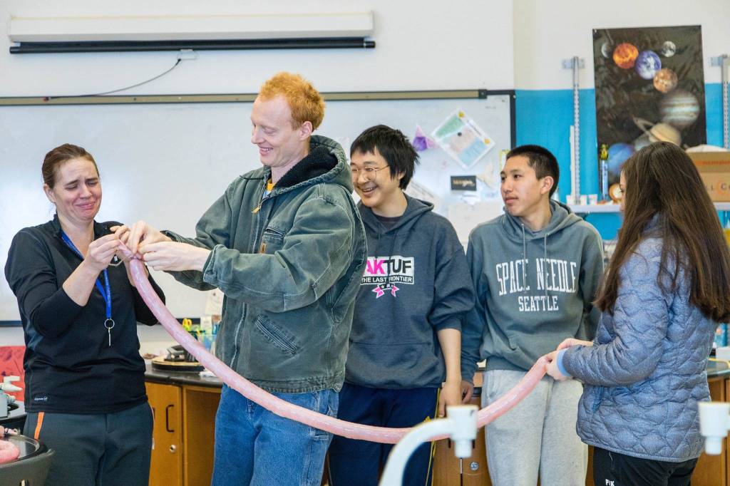 Photos by Erin Irwin/Education Week                                Kristian Nattinger, center, a former chemistry teacher at Scammon Bay School, helps tie off an inflated seal intestine as visiting math teacher Ellen Piekarski grimaces. Seal intestines are inflated, dried, and made into a traditional Yupik raincoat.