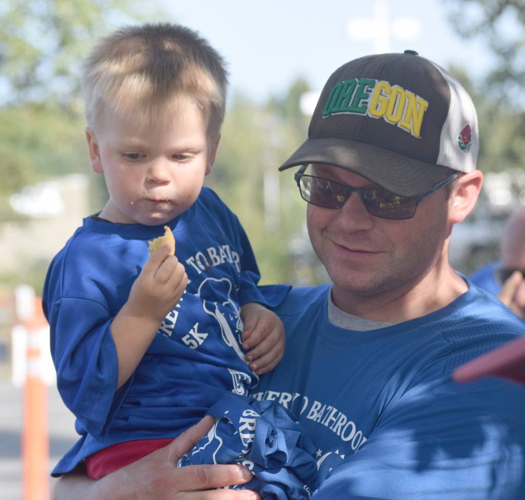 Mason Warfle, 2, is held by his father, Kenais Jason Warfle, at the Kenai Lions Club aid station at the halfway point of the Brewery to Bathroom .5K The race for the rest of us on Sunday, Aug. 11, 2019, in Soldotna, Alaska. (Photo by Jeff Helminiak/Peninsula Clarion)