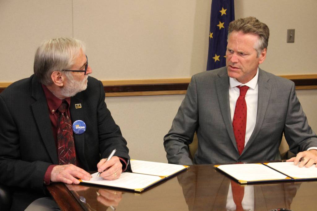 University of Alaska Board of Regents chairman John Davies, left, and Gov. Mike Dunleavy sign an agreement, Tuesday, Aug. 13, 2019, in Anchorage, Alaska, that will spread $70 million in cuts to the university system over three years. That is a sharp reversal from the $135 million cut Dunleavy earlier proposed for this year. (AP Photo/Mark Thiessen)