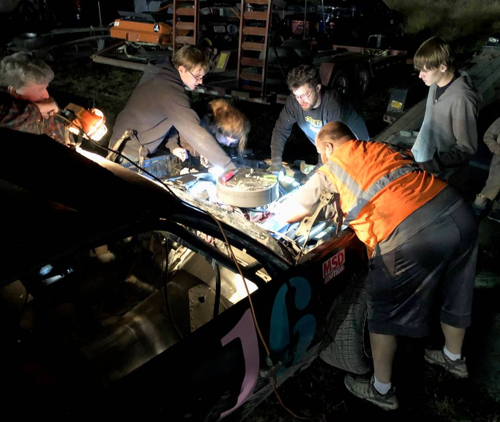 A crew of racers, mechanics and friends pore over the engine of Gracie Bass No. 16 A-Stock racer Friday, Sept. 6, 2019, at Twin City Raceway in Kenai, Alaska. (Photo by Joey Klecka/Peninsula Clarion)