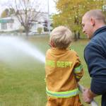 A young firefighter-in-training practices knocking down a water jug with a fire hose during the Central Emergency Services Open House at Fire Station 1 in Soldotna, Alaska on Sept. 28, 2019. (Photo by Brian Mazurek/Peninsula Clarion)