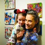 Carla Cope and her daughter, Nova, pose next to their paintings at left at the Nov. 8, 2019, opening of the 10x10 show at Bunnell Street Arts Center in Homer, Alaska. Nova painted the background elements to the paintings and her mother added to that. (Photo by Michael Armstrong/Homer News)