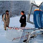 This Jan. 9, 2020 photo provided by Alaska State Troopers shows Tyson Steele, left, talking with Helo 3 Tactical Flight Officer Zac Johnson after Steeles rescue from outside Susitna Valley, Alaska. Troopers rescued Tyson Steele, 30, who survived in a makeshift shelter after his remote cabin burned last month, after spotting him and an SOS sign in the snow. (Alaska State Troopers via AP)