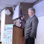 Dave Stieren, community outreach director for Gov. Mike Dunleavy, holds his phone up to the microphone as Dunleavy gives a remote speech to the Kenai and Soldotna Chambers of Commerce at the Soldotna Regional Sports Complex on Monday, March 9, 2020. (Photo by Brian Mazurek/Peninsula Clarion)