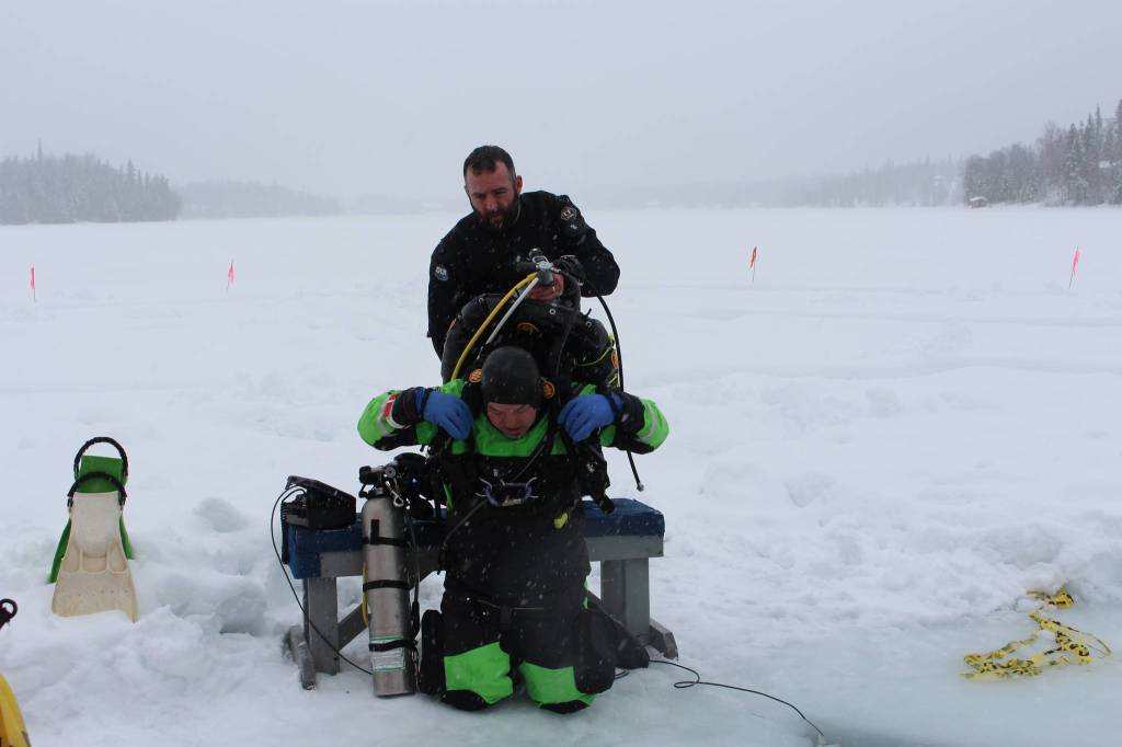 Tony Gillham helps Stephen Robertson suit up for an ice dive on Island Lake in Nikiski, Alaska on March 21, 2020. (Photo by Brian Mazurek/Peninsula Clarion)