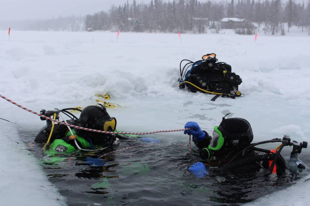 Stephen Robertson, left, and T.J. Cox, right, dive into Island Lake in Nikiski, Alaska on March 21, 2020. (Photo by Brian Mazurek/Peninsula Clarion)