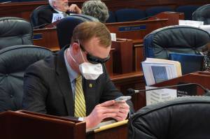 Alaska state Rep. David Eastman sits at his desk on the House floor in Juneau, Alaska, Monday, March 23, 2020. Eastman, a Wasilla Republican, has been critical of the Legislatures planning around the coronavirus. Rep. Sharon Jackson also wore a mask on the House floor Monday. (AP Photo/Becky Bohrer)