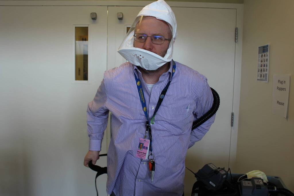 Shayne Pond, Emergency Department Director for Central Peninsula Hospital, demonstrates how to put on a PAPR – Powered air purifying respirator – on April 7, 2020. (Photo by Brian Mazurek/Peninsula Clarion)                                Shayne Pond, Emergency Department Director for Central Peninsula Hospital, demonstrates how to put on a PAPR  Powered air purifying respirator  on Tuesday.
