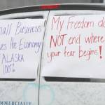 A commercial van with signs on its back windows is driven through downtown Anchorage, Alaska, Wednesday, as part of a caravan of more than 80 vehicles. Participants urged local and state leaders to open up businesses shuttered temporarily while residents were told to stay home. The state will allow some businesses to open Friday, and the city of Anchorage will allow some Monday. (AP Photo/Mark Thiessen)