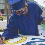 Kenai Alternative High School graduate Elsie Daniels signs the ceiling tile for the Class of 2020 at the KAHS graduation Monday in Kenai, Alaska. The tile will join other graduating classes in the ceiling of the school office. (Photo by Jeff Helminiak/Peninsula Clarion)