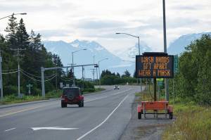 Cars pass the City of Homer advisory signs on Wednesday morning, June 24, 2020, at Mile 172 Sterling Highway near West Hill Road in Homer, Alaska. The sign also reads Keep COVID-19 out of Homer. (Photo by Michael Armstrong/Homer News)