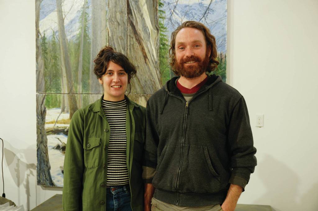 Elissa and David Pettibone pose on Oct. 16, 2018, by one of David Pettibones paintings at The Shop, an art space the Pettibones started in August 2018 in Kachemak City, Alaska. (Photo by Michael Armstrong/Homer News)