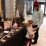 Remmy Rutledge, center, and her mom Breanna Rutledge, right, of Sterling, check out Remmys new ornament purchased from Kenai Kombucha owner Devon Gonzales, left, during the Merry Little Christmas Market at the Peninsula Center Mall in Soldotna, Alaska, on Nov. 7, 2020. (Photo by Brian Mazurek/Peninsula Clarion)