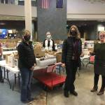 Members of the Juneau Education Support Staff union pose for a photo in front of meals being prepared for kids in Juneau as Catherine Pusich, 2nd from right, hands a check from the union to Adrianne Schwartz to clear all money owed for school meals at Thunder Mountain High School on Dec. 21, 2020. (Michael S. Lockett / Juneau Empire)