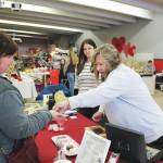 Photo by Brian Mazurek/Peninsula Clarion 
Robin Hahn, left, of Soldotna buys some hot cocoa bombs from Sherian Soares, right, and Ashley Soares, center, owners of Bennys Sweets and Beyond, at a Valentines Bazaar in Soldotna on Saturday.