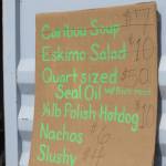 This July 4, 2014, photo provided by Val Kreil shows a restaurant menu of food for sale, including Caribou soup, Eskimo Salad and Seal Oil at the community fairgrounds in Kotzebue, Alaska. The Maniilaq Health Association in the Chukchi Sea community of Kotzebue has received state approval to process and serve seal oil at its elder care facility in Kotzebue, believed to be a first for seal oil in the U.S. (Val Kreil via AP)