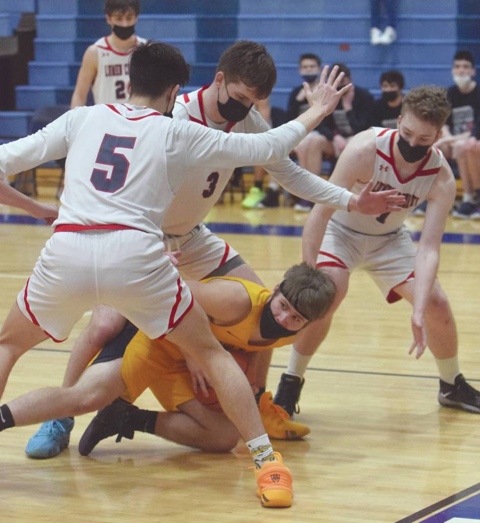 Ninilchiks Cole Hadro is surrounded by Noah Cruz, Daniel Bennett and Tim Bennett of Lumen Christi on Friday, March 19, 2021, in the Peninsula Conference championship game at Soldotna High School in Soldotna, Alaska. (Photo by Jeff Helminiak/Peninsula Clarion)