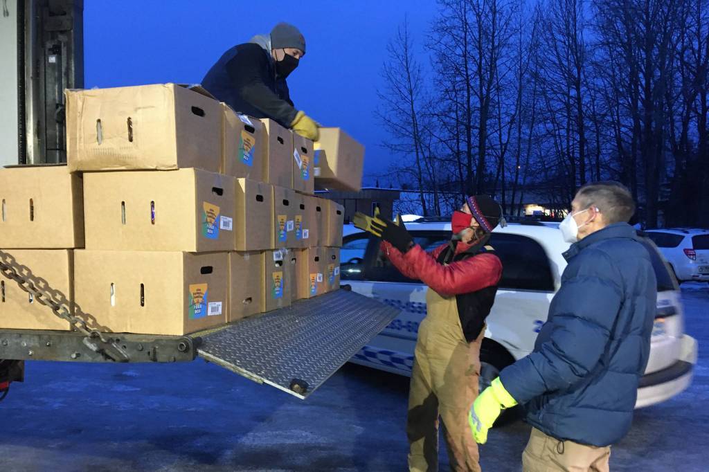 Todd Duwe hands a food box to Brad Nyquist as Mark Larson looks on Tuesday, Dec. 22, 2020, at Christ Lutheran Church in Soldotna, Alaska. The church volunteers were distributing food from the United States Department of Agricultures Farmers to Families Food Box Program, delivered by the Kenai Peninsula Food Bank. The food bank saw a surge in demand last year due to the coronavirus pandemic. (Photo by Jeff Helminiak/Peninsula Clarion)