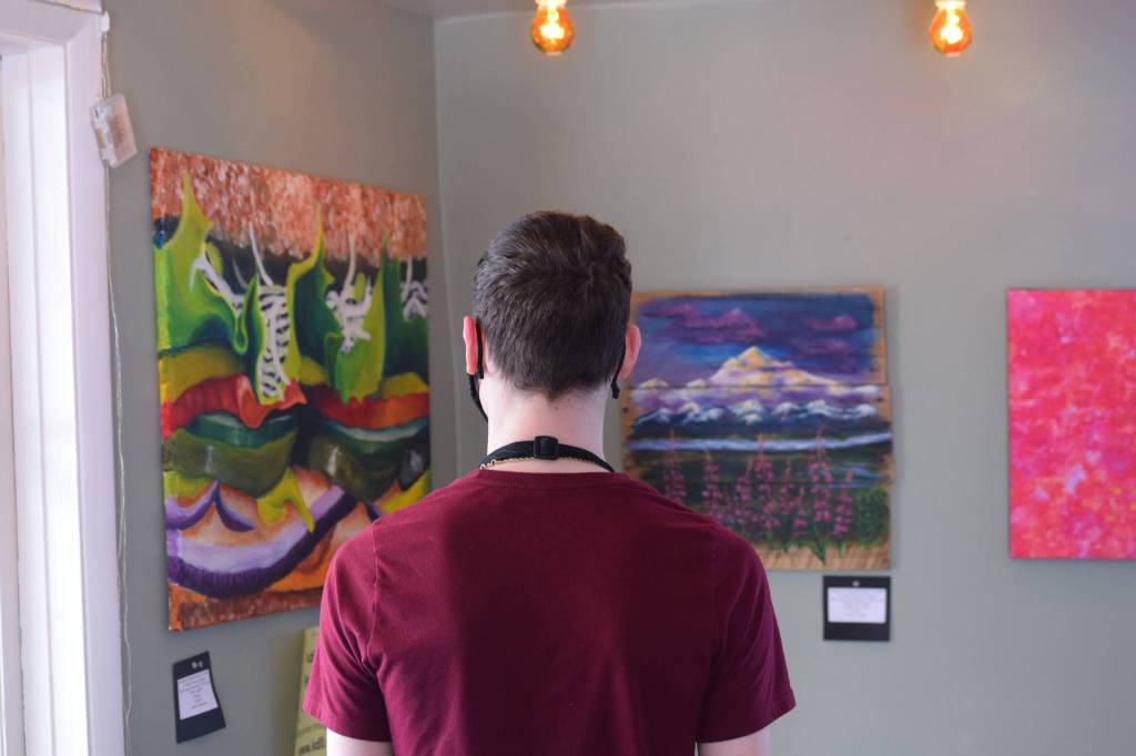Samuel Anderson examines artwork up for bid while on shift at Veronicas Cafe on April 7, 2021. The Kenai Fine Art Center and KDLL Public Radio are auctioning off local art through the month of April. (Photo by Camille Botello/Peninsula Clarion)