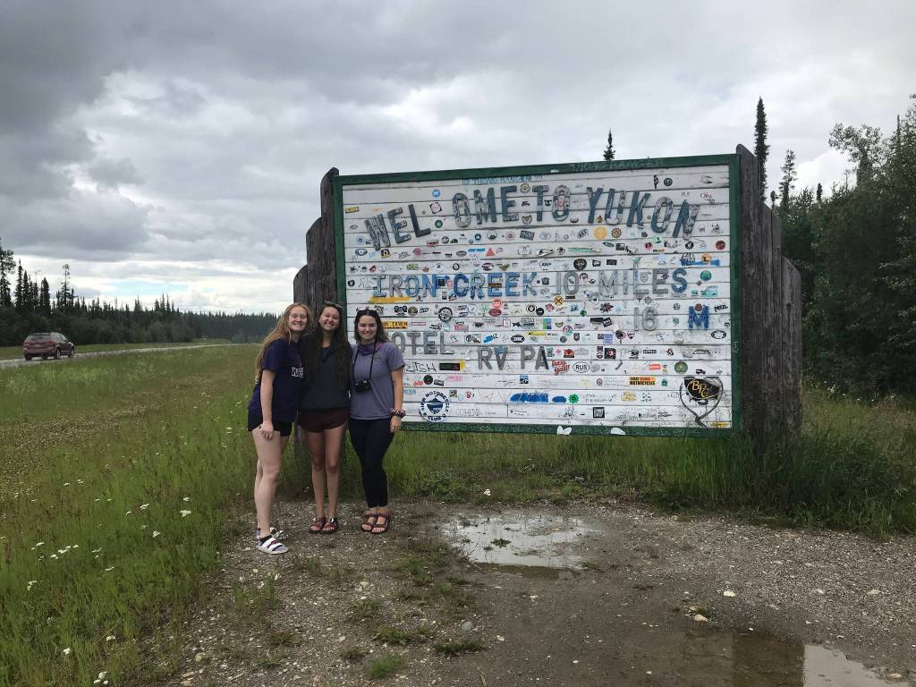 From left to right: Camille Botello, Emma Schoonover and Grace Thompson-Johnston stand in front of a sign welcoming them to the Yukon territory in Canada as they make their way up the Alaska Highway on July 16, 2020. (Photo provided)