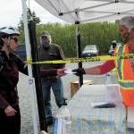 Margarida Kondak, right, hands a visitor a mask before she walks in at the Homer Farmers Market entrance on Saturday, May 30, 2020 in Homer, Alaska. (Photo by Megan Pacer/Homer News)