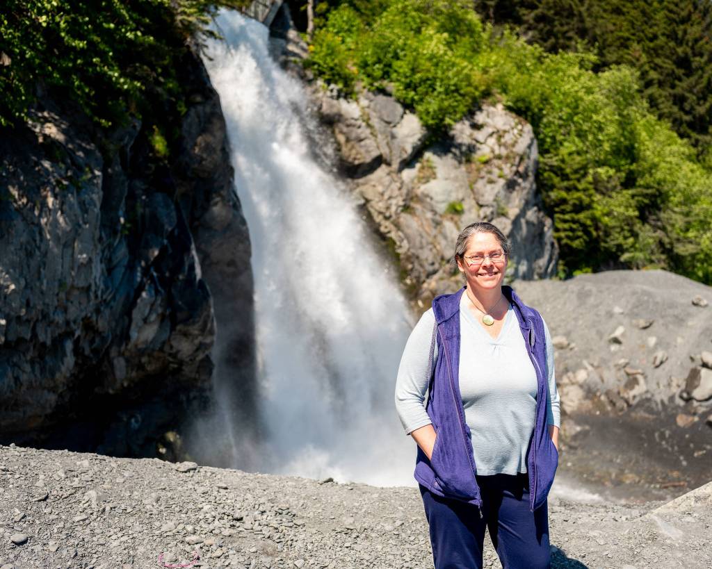 In June 2021, Stephanie Presley, program lead for the Seward-Bear Creek Flood Service Area, stands in front of the Lowell Creek waterfall, which is caused by one of Sewards most important flood mitigation efforts to divert Lowell Creek away from the center of town and tunnel it directly into nearby Resurrection Bay. (Young Kim for The Hechinger Report)