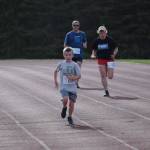 Gus Reimer crosses the finish line in front of Adam Reimer and Julie Laker during the first race of the Salmon Run Series at Skyview Middle School on Wednesday, July 7, 2021. (Camille Botello / Peninsula Clarion)