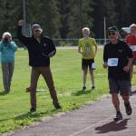 Kenai Watershed Forum Stream Watch Intern Brandom Drzazgowski cheers on Henry Lachowski as he crosses the finish line during the first race of the Salmon Run Series at the Skyview Middle School track on Wednesday, July 7, 2021. (Camille Botello / Peninsula Clarion)