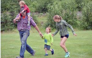 Chad Anderson of Kasilof and Allie Ostrander guide Everett Anderson, 3, to the finish line Wednesday, July 19, 2017, at the Salmon Run Series at Tsalteshi Trails. Getting the free ride on Chads shoulders is Ben Anderson, 2. (Photo by Jeff Helminiak/Peninsula Clarion)