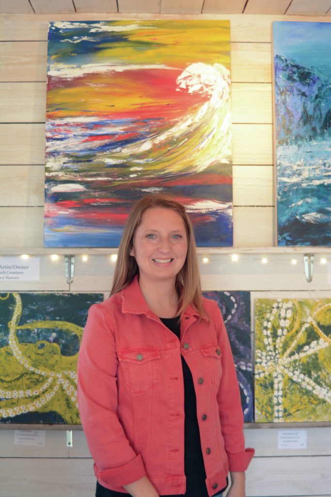 Tracy Hansen poses for a photo in front of her paintings at her Ocean Drive shop, 59 North, on Tuesday, Aug. 10, 2021, in Homer, Alaska. (Photo by Michael Armstrong/Homer News)