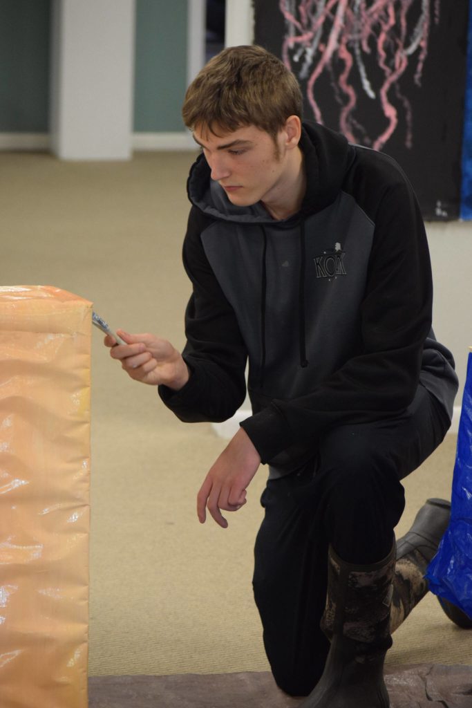 Jacob Bayhi paints a podium for the Kenai Alternative High Schools mural installation at the Kenai Art Center on Tuesday, Nov. 9, 2021. (Camille Botello/Peninsula Clarion)
