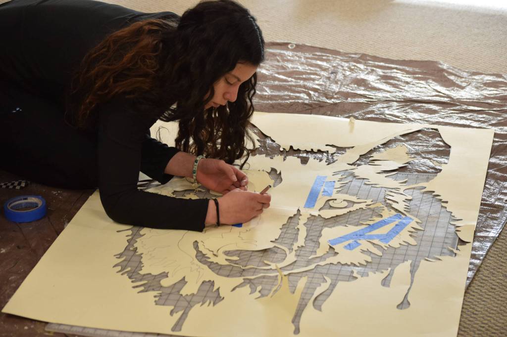 Tatihana DeHoyos cuts out the centerpiece stencil for the Kenai Alternative High Schools mural installation at the Kenai Art Center on Tuesday, Nov. 9, 2021. (Camille Botello/Peninsula Clarion)