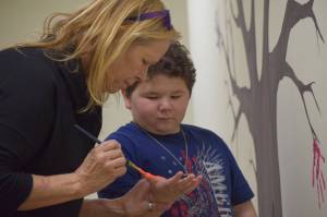 Carolyn Massey paints 10-year-old Kenny Smiths hand to add to the helping hands tree at the Childrens Advocacy Center on Tuesday, Nov. 16, 2021, in Kenai, Alaska. (Camille Botello/Peninsula Clarion)