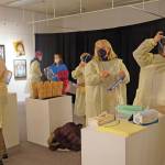 Visitors put on personal protective equipment before an artist talk by Dr. Sami Ali at the Jan. 7, First Friday opening of her exhibit, The Mind of a Healthcare Worker During the COVID-19 Pandemic, at the Homer Council on the Arts in Homer. (Photo by Michael Armstrong/Homer News)