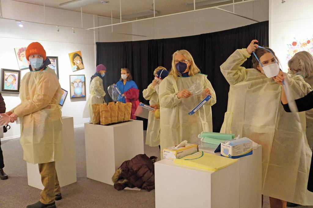 Visitors put on personal protective equipment before an artist talk by Dr. Sami Ali at the Jan. 7, First Friday opening of her exhibit, The Mind of a Healthcare Worker During the COVID-19 Pandemic, at the Homer Council on the Arts in Homer. (Photo by Michael Armstrong/Homer News)