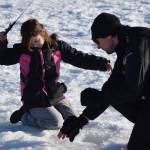 Lucas Stumpf, a fishery biologist with the Division of Sport Fish, helps Aurora Borealis Charter School third grader Teagan Jorgensen, left, with her line while she ice fishes at Sport Lake in Soldotna as part of the Alaska Department of Fish and Game’s “Salmon in the Classroom” ice fishing educational program on Wednesday, March 2, 2022, in Soldotna, Alaska. (Camille Botello/Peninsula Clarion)