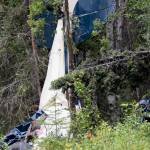 In this July 31, 2020, file photo, a plane rests in brush and trees outside of Soldotna, Alaska, after a midair collision that killed seven people, including State Rep. Gary Knopp. A Feb. 22 report by the National Transportation and Safety Board is recommending that all pilots be required to communicate their positions on a designated radio frequency when entering and exiting areas not controlled by air traffic control towers throughout Alaska. (Jeff Helminiak/Peninsula Clarion via AP, F-le)