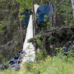 In this July 31, 2020, file photo, a plane rests in brush and trees outside of Soldotna, Alaska, after a midair collision that killed seven people, including State Rep. Gary Knopp. A Feb. 22 report by the National Transportation and Safety Board is recommending that all pilots be required to communicate their positions on a designated radio frequency when entering and exiting areas not controlled by air traffic control towers throughout Alaska. (Jeff Helminiak/Peninsula Clarion via AP, F-le)