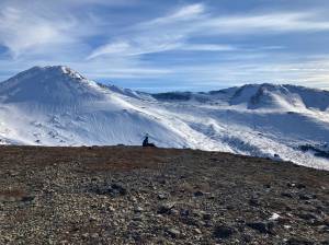 A hiker rests near the peak of Near Point Trail in Anchorage, Alaska, on March 20, 2022. (Camille Botello/Peninsula Clarion)