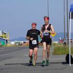 Shaun Marshall-Pryde, left, and Stirling Marshall-Pryde, right, finish together the 2022 Homer Spit Run, on Saturday, June 25, 2022, at the End of the Road Park in Homer, Alaska. (Photo by Michael Armstrong/Homer News)