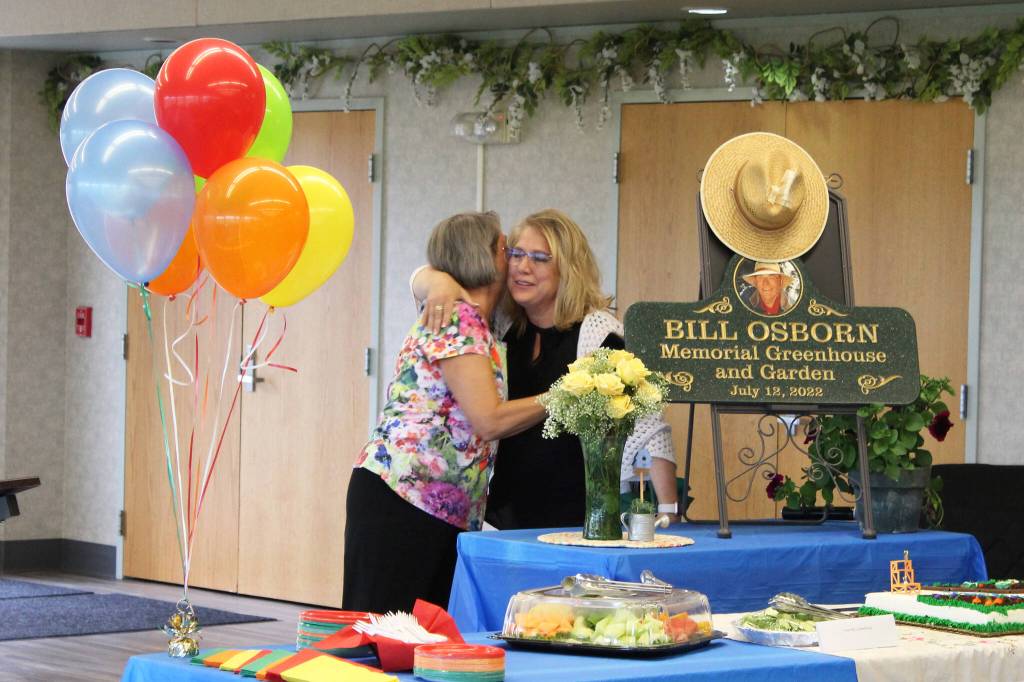 Vicke Kukowski (left) hugs Kathy Romain (right) after unveiling a plaque dedicating the Kenai Senior Centers greenhouse to Bill Osborn during a ceremony on Tuesday, July 12, 2022 in Kenai, Alaska. (Ashlyn OHara/Peninsula Clarion)