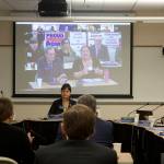 Amanda Triplett, at right on overhead screen, discusses the University of Alaskas Did You Know program while faculty members in the background hold up signs protesting a labor contract stalemate during the Board of Regents meeting Friday in Juneau. The program highlights cooperative efforts the university is participating in with communities such as workplace experience and dual enrollments with other educational institutions. (Mark Sabbatini / Juneau Empire)