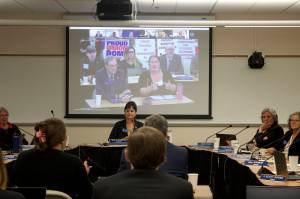 Amanda Triplett, at right on overhead screen, discusses the University of Alaskas Did You Know program while faculty members in the background hold up signs protesting a labor contract stalemate during the Board of Regents meeting Friday in Juneau. The program highlights cooperative efforts the university is participating in with communities such as workplace experience and dual enrollments with other educational institutions. (Mark Sabbatini / Juneau Empire)